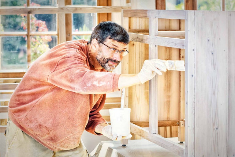 Un homme peint une armoire en bois avec un pinceau.