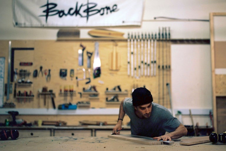 Mann misst ein Holzbrett in einer Werkstatt mit Werkzeugen an der Wand
