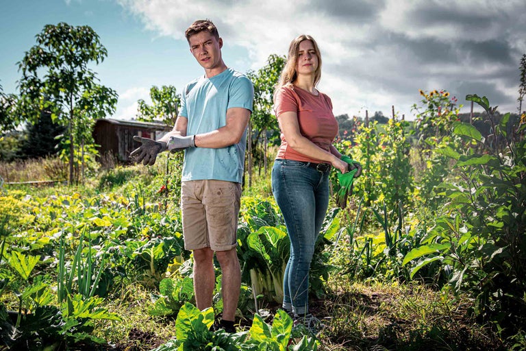 Un couple dans le potager avec des gants de jardinage et des légumes.