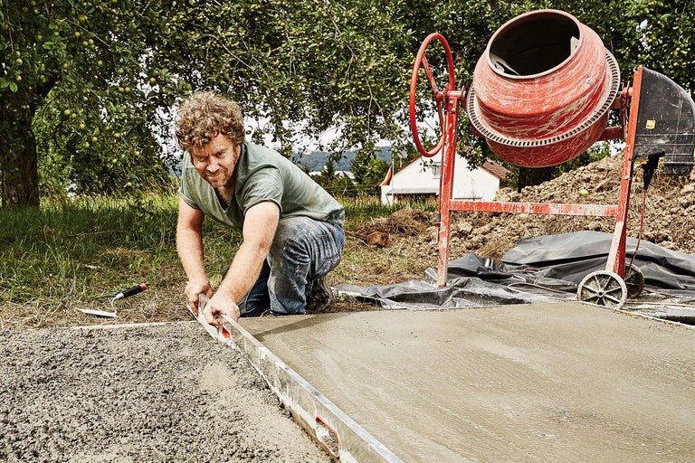 Un homme lisse le béton à la règle près d'une bétonnière