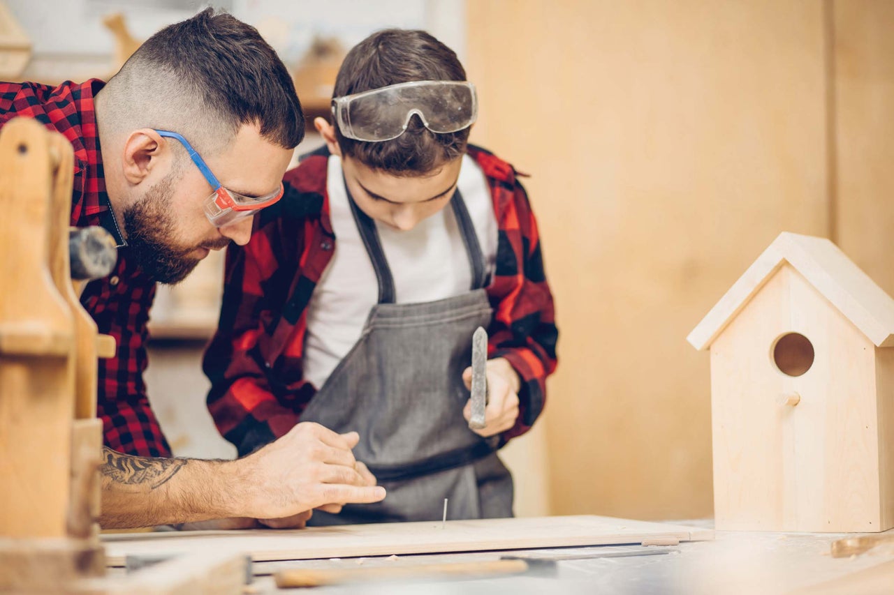 Vater und Sohn bauen gemeinsam ein Vogelhaus mit Hammer und Nagel.
