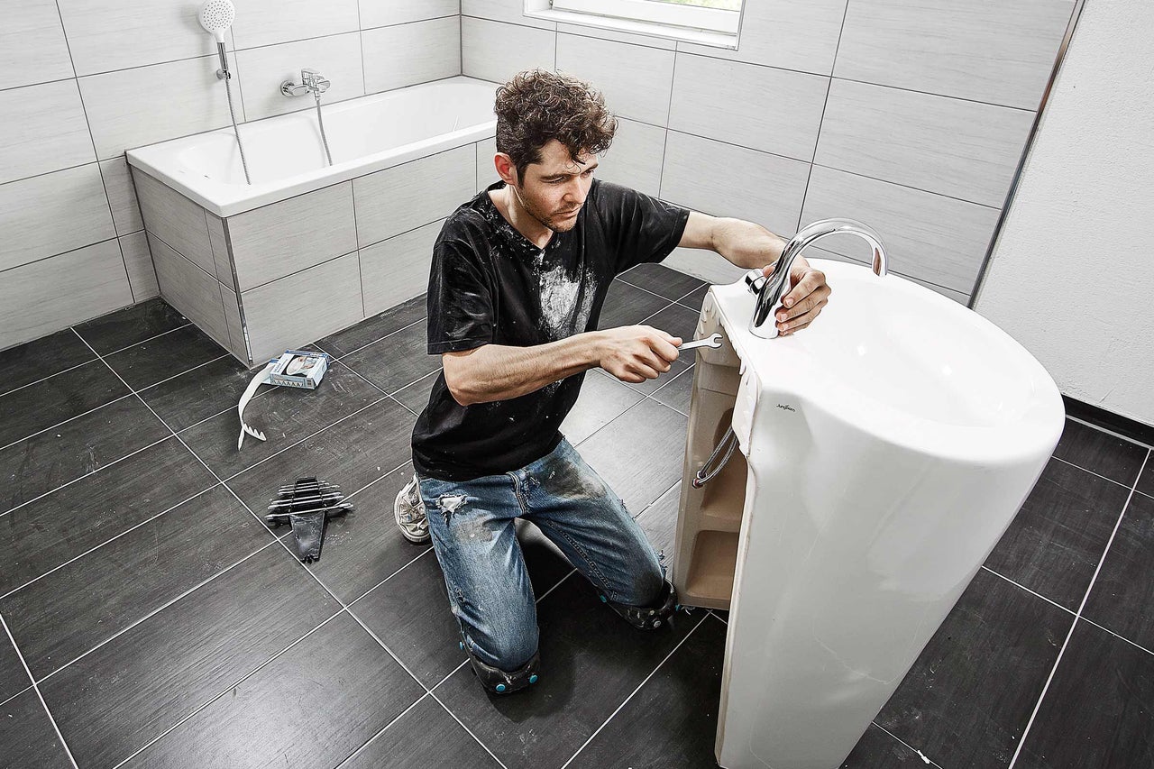 Installateur installant un lavabo dans une salle de bains avec robinetterie et outils.