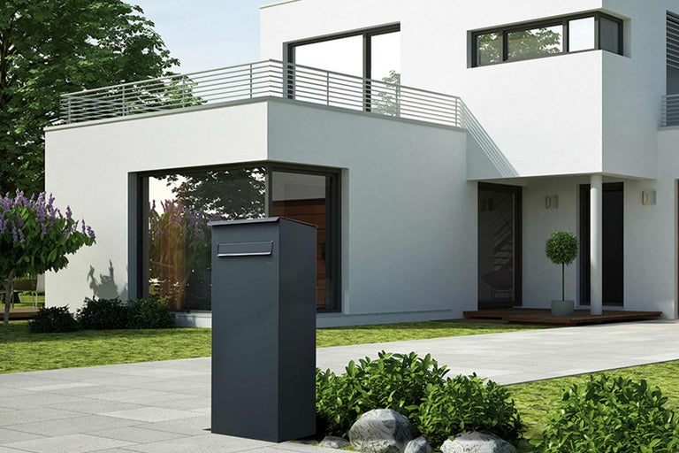 Freistehender Briefkasten vor einem modernen Haus mit Garten