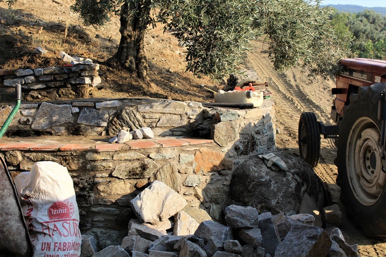 Steinmauerbau mit Steinen, Traktor und Baum im Garten