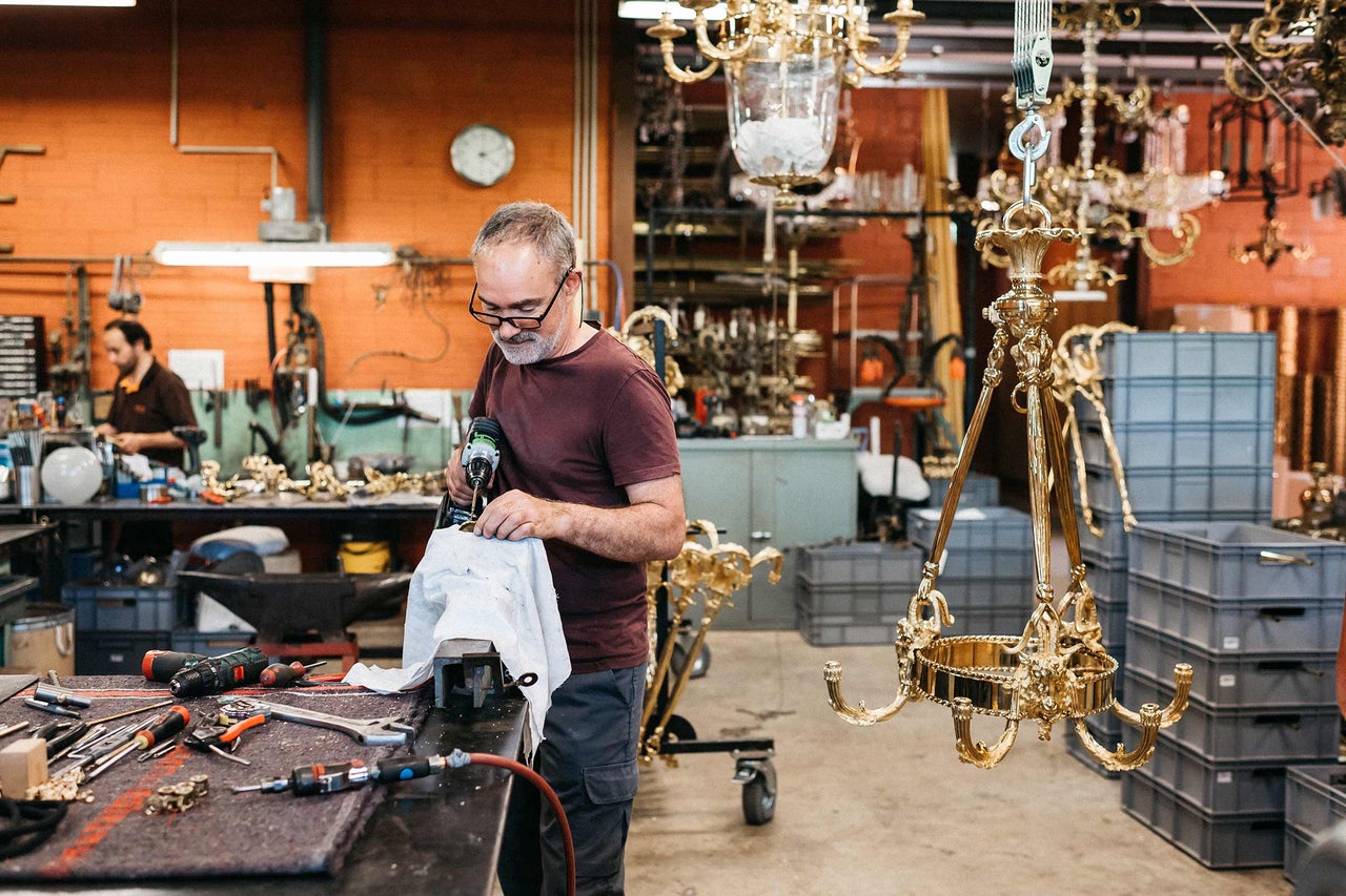 Un homme travaille sur un lustre doré dans un atelier avec des outils.