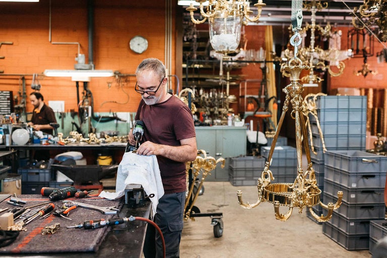 Un homme travaille sur un lustre doré dans un atelier avec des outils.