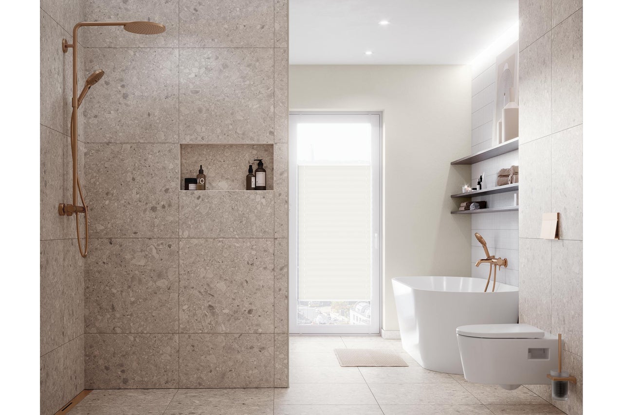 Salle de bains moderne et lumineuse avec douche à l'italienne effet pierre, baignoire en îlot, toilette suspendue et robinetterie en cuivre.