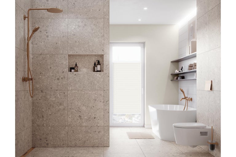 Salle de bains moderne et lumineuse avec douche à l'italienne effet pierre, baignoire en îlot, toilette suspendue et robinetterie en cuivre.