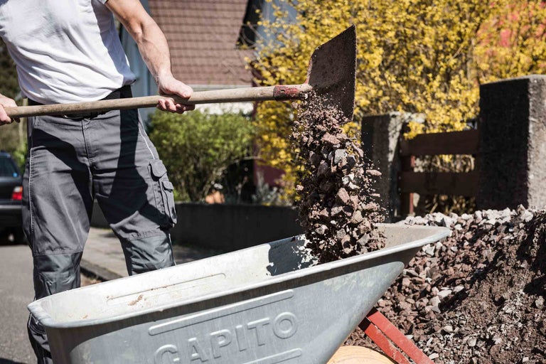 Mann schaufelt Kies in eine Schubkarre