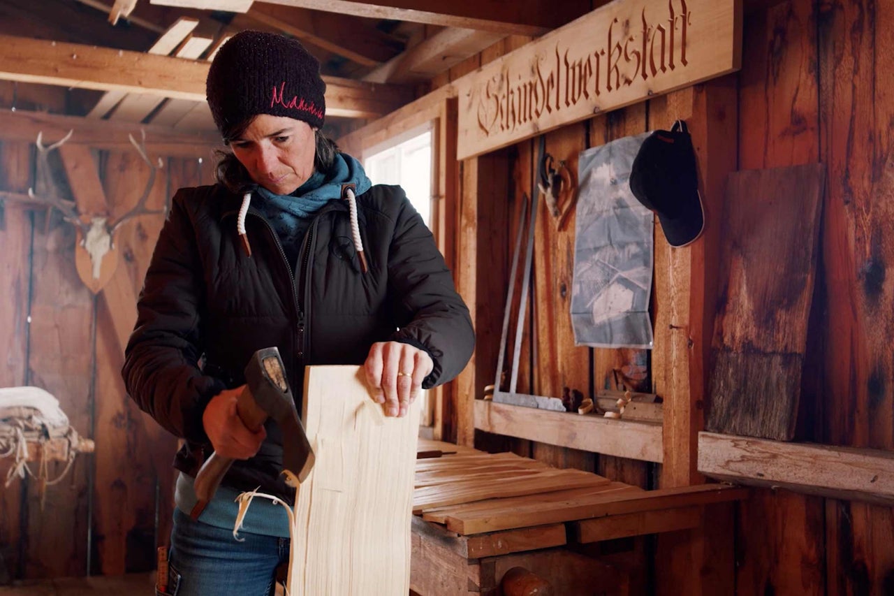 Une femme travaille avec une hache dans un atelier de menuiserie sur une planche de bois.