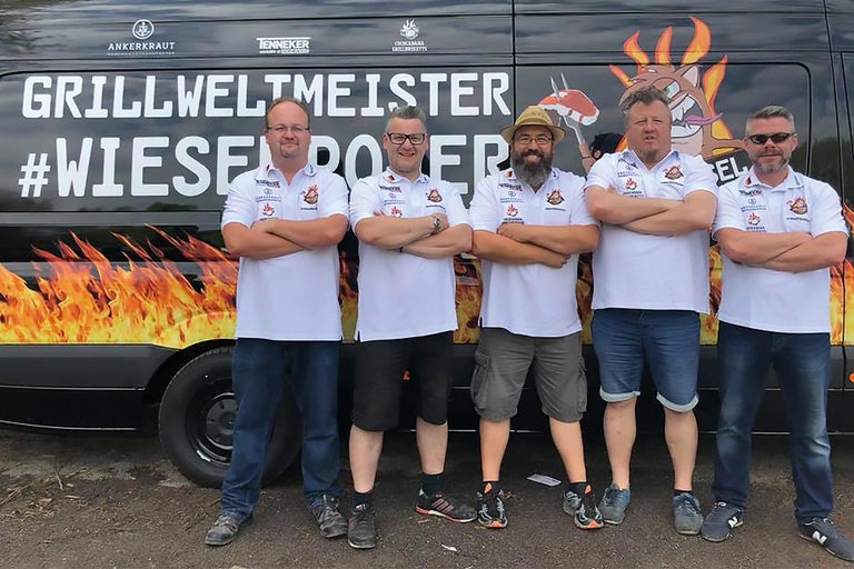 Cinq personnes devant un bus Grill World Champion avec un motif de flammes