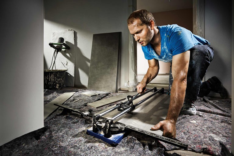 Fliesenleger mit Fliesenschneider bei der Arbeit auf einer Baustelle