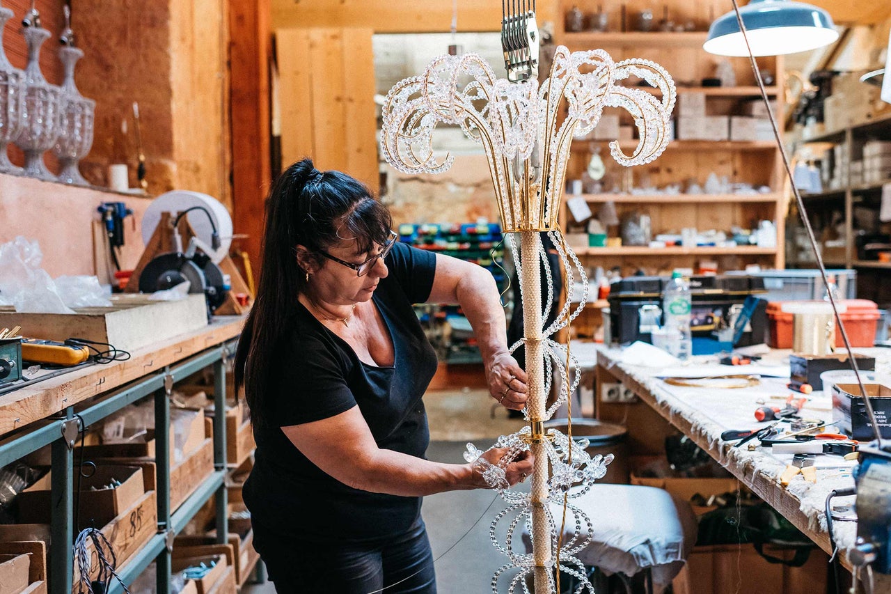 Une femme assemble un lustre en cristal dans un atelier.