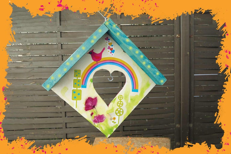 Dekoratives Vogelhaus mit herzförmiger Öffnung, verziert mit Aufklebern und Malereien.