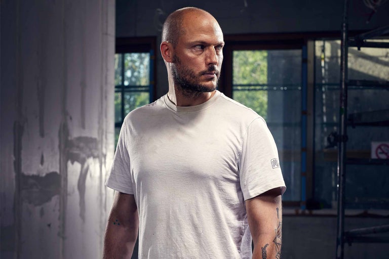 Homme avec des tatouages et un t-shirt court dans un bâtiment en construction