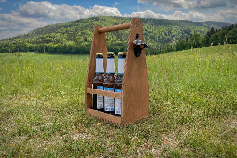 Holzbierträger mit Bierflaschen und Flaschenöffner vor einer Wiese