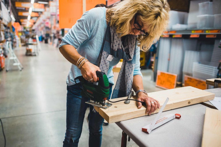 Une femme scie une planche de bois avec une scie sauteuse dans le magasin de bricolage Hornbach.