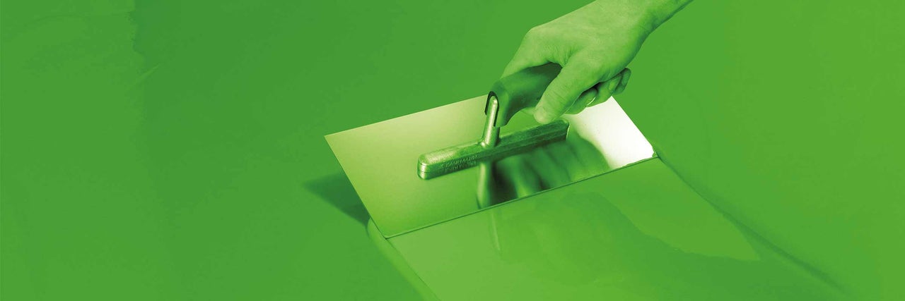 Une main tient une truelle lors de l'application de la chape.
