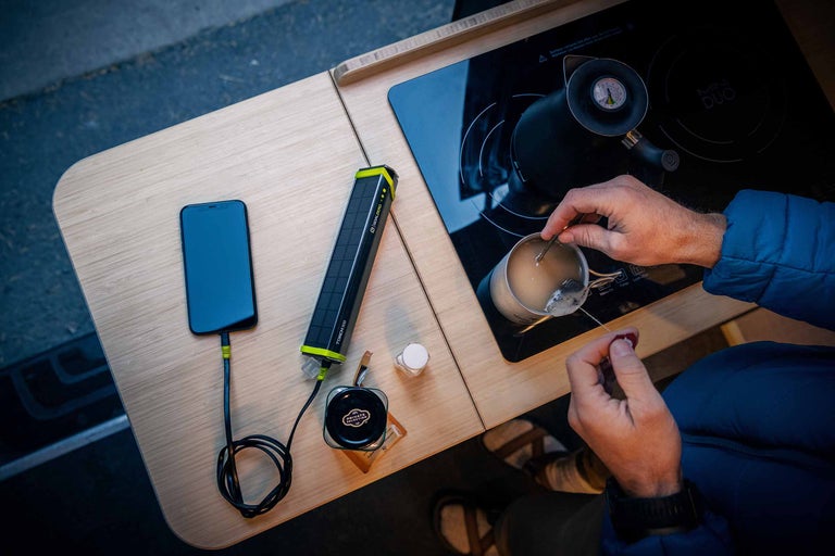 Szene mit Smartphone, Goal Zero Torch 500 Solarladegerät, Kochfeld, Teekessel und Person, die Tee zubereitet