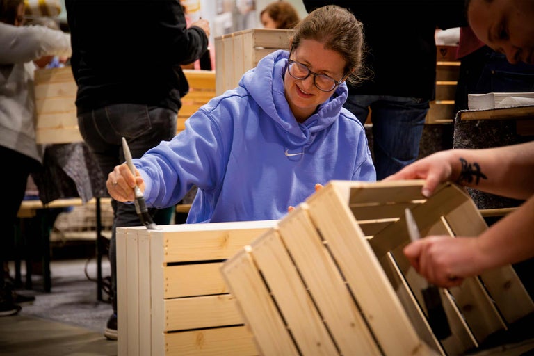Person streicht eine Holzkiste mit einem Pinsel