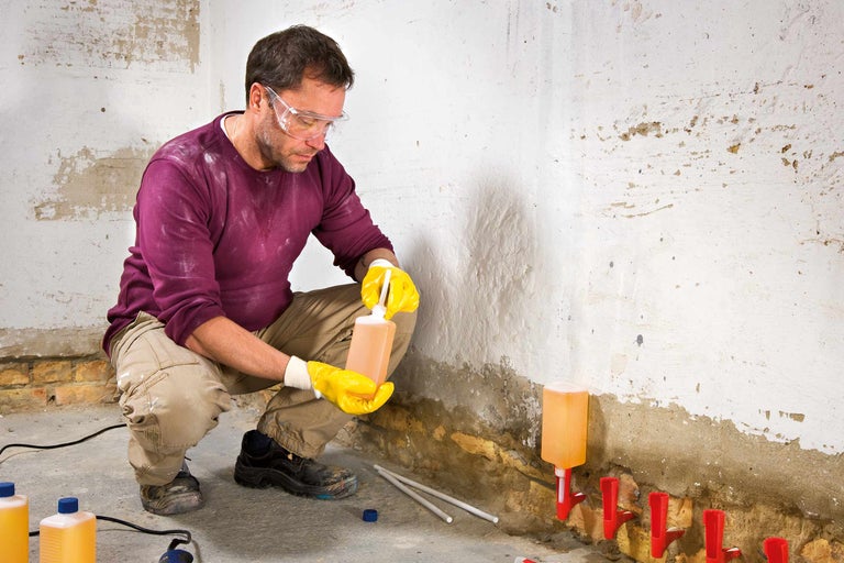 Homme injectant une barrière horizontale dans un mur, portant des lunettes de protection et des gants