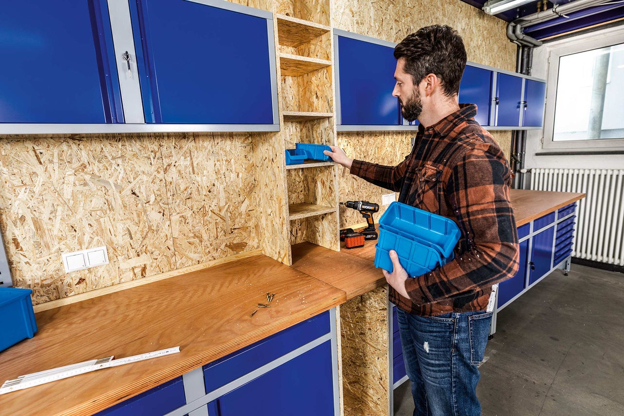 Aménagement d'atelier avec établi, étagères, armoires et un homme plaçant une boîte de rangement