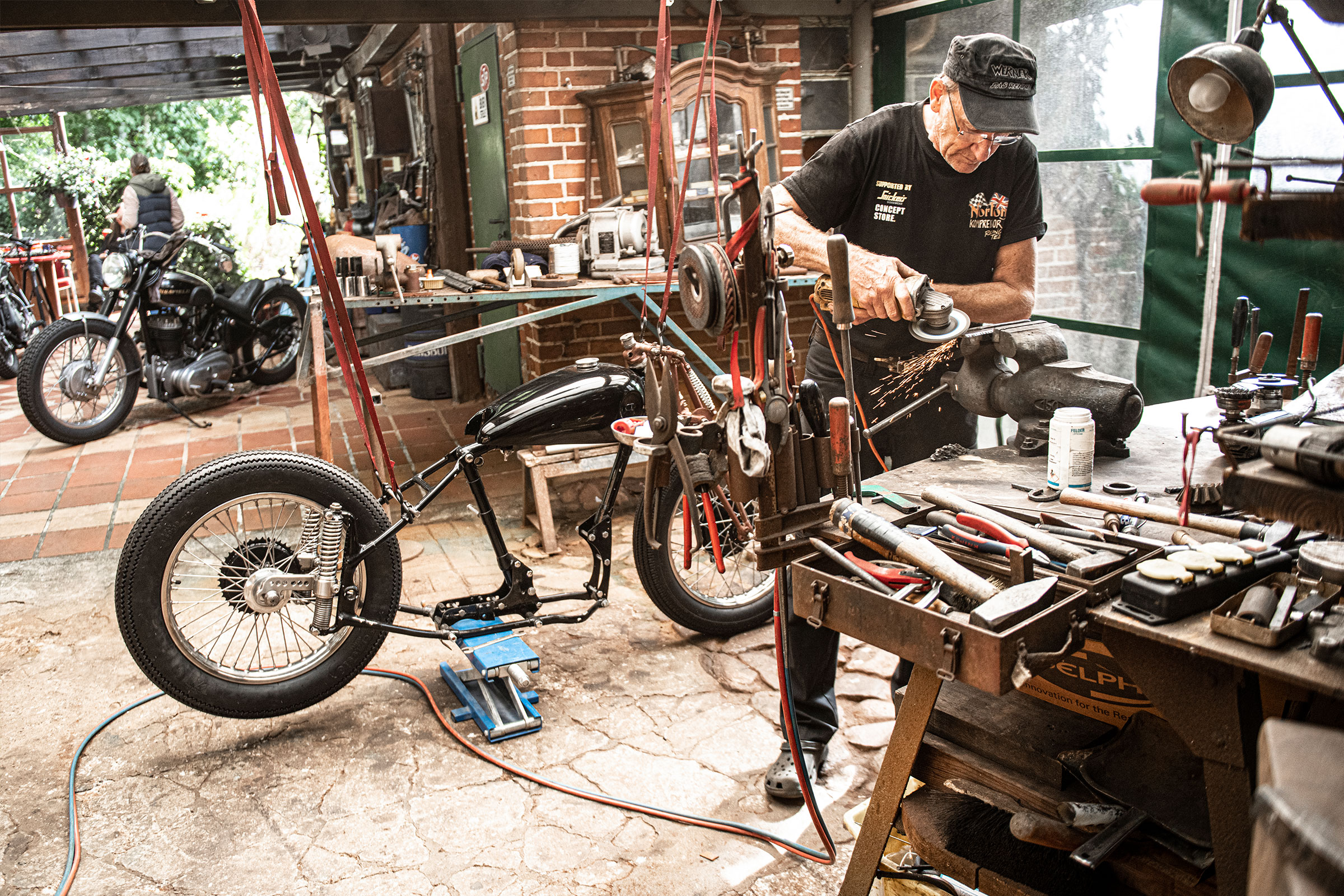 Werkstatt mit Motorrad, Werkbank und Handwerker bei der Arbeit.