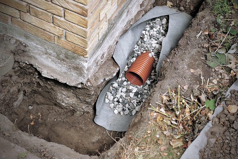 Fossé de drainage avec tuyau de drainage et gravier pour protéger un bâtiment.