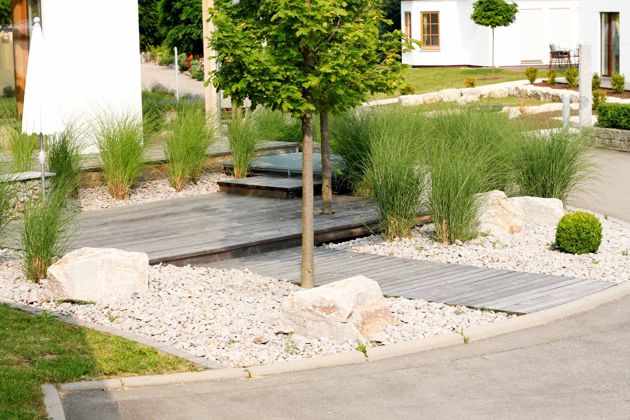 Gestalteter Gartenbereich mit Holzterrasse, Zierkies und Bepflanzung