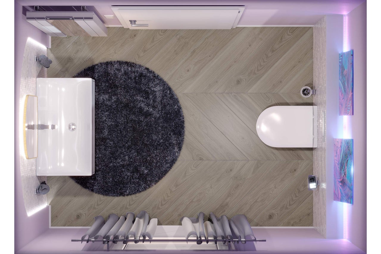 Vue de dessus d'une salle de bains moderne avec sol aspect bois en chevrons, tapis rond, lavabo blanc et WC suspendu.