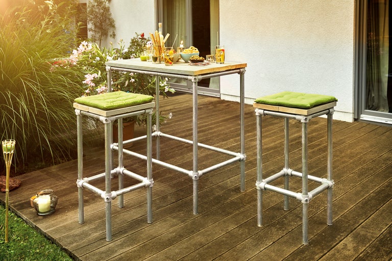 Scène de jardin avec table haute et deux tabourets de bar en tube métallique et éléments en bois