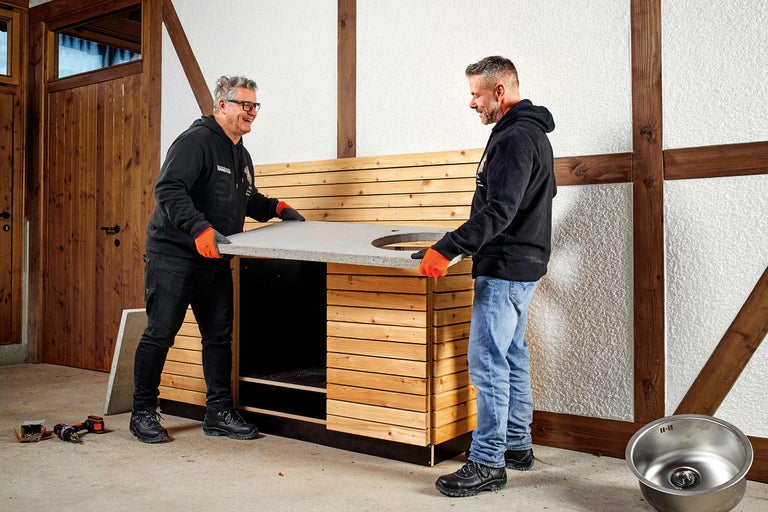 Deux artisans montent une cuisine d'extérieur avec un revêtement en bois et un plan de travail en béton