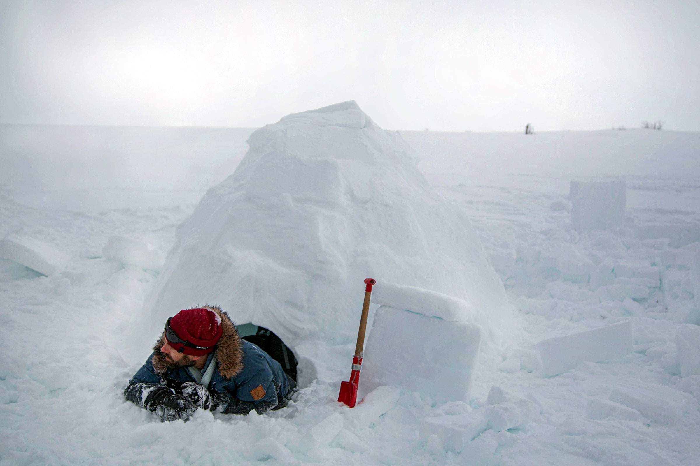 Mann baut Iglu mit Schaufel im Schnee