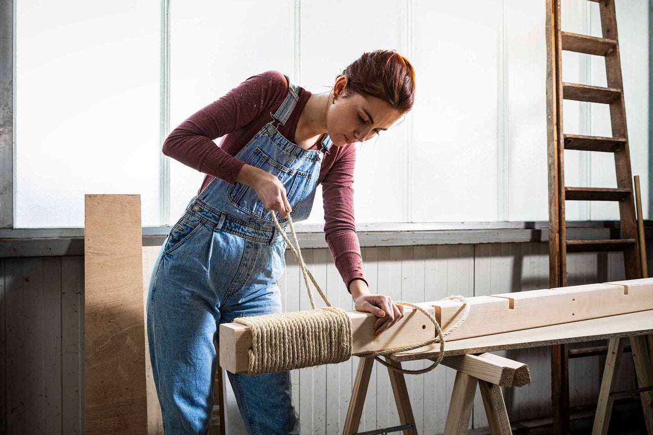 Frau umwickelt ein Holzstück mit einer Seilschnur auf einem Holztisch