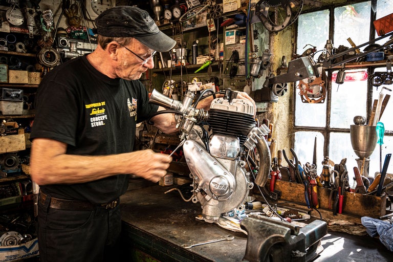 Mann arbeitet an Motorradmotor in Werkstatt mit Werkzeugen.