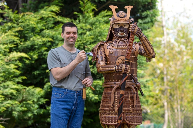 Mann steht neben einer Samurai-Rüstung aus Holz.