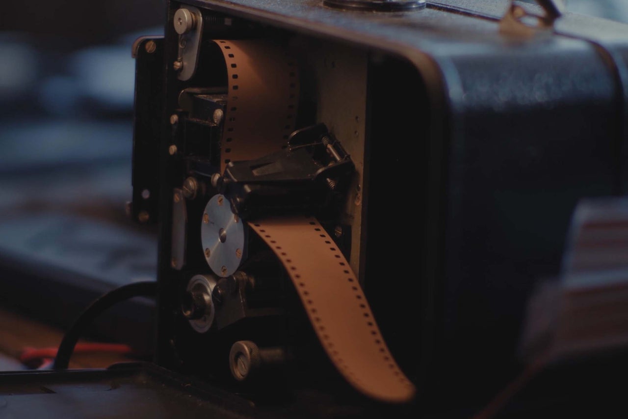 Gros plan d'un projecteur de film analogique avec une pellicule insérée à l'intérieur du boîtier ouvert.