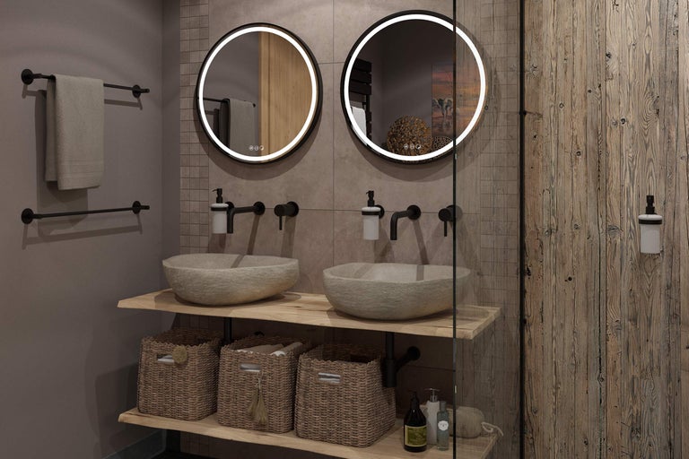 Salle de bains moderne avec deux miroirs LED ronds, vasques en pierre sur plateau en bois, robinetterie noire et paniers tressés.