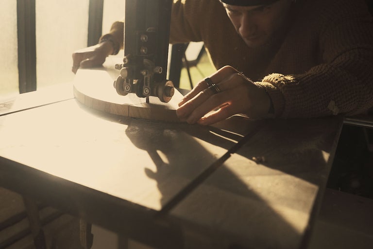 Artisan travaillant avec une scie à ruban sur une pièce de bois.
