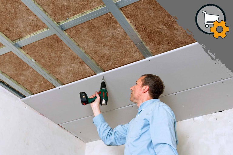 Un homme installe un plafond en placoplâtre avec un tournevis sans fil sur une sous-structure avec de la laine isolante