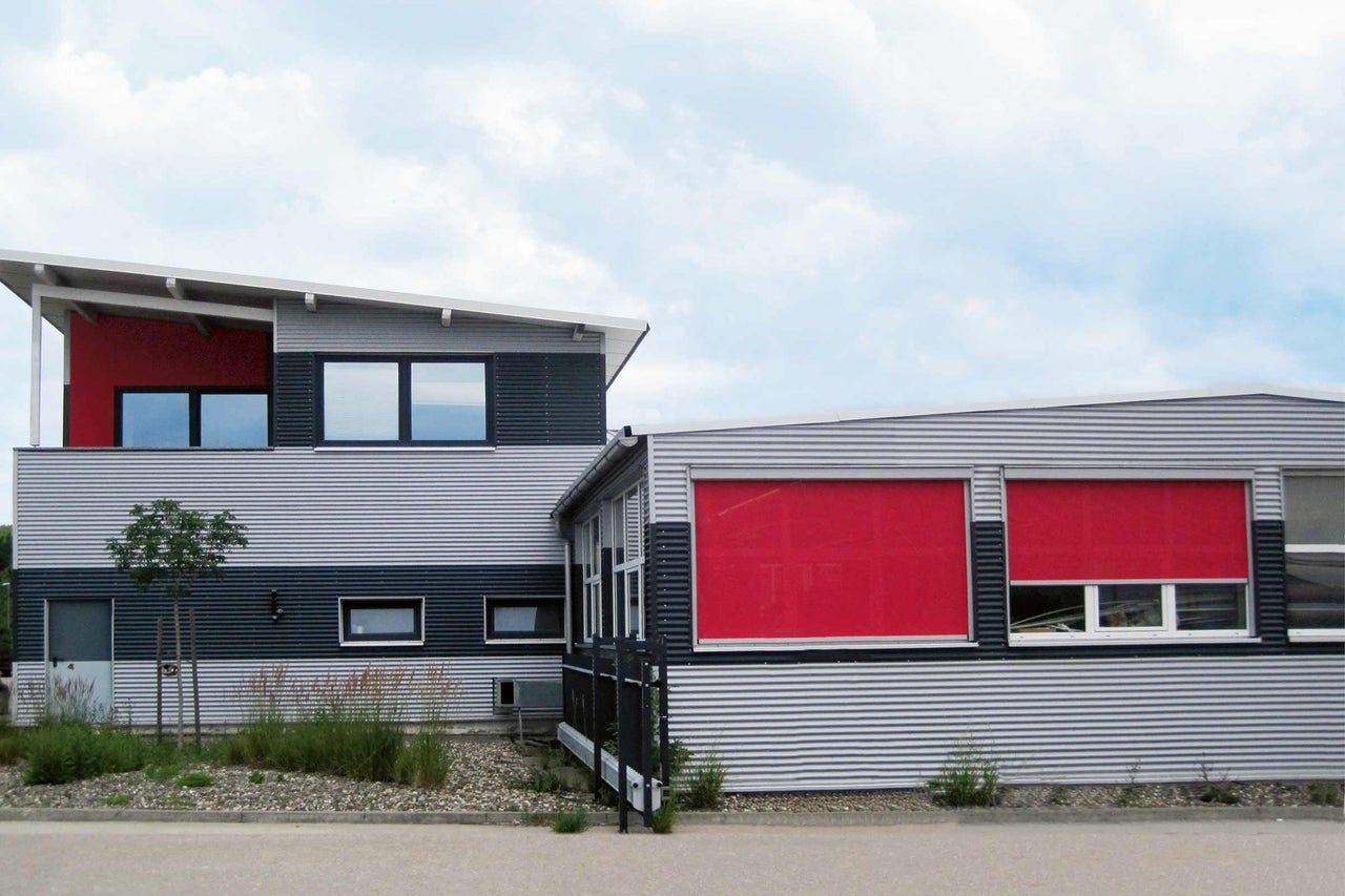 Gebäude mit rotem Sonnenschutzsystem vor den Fenstern.