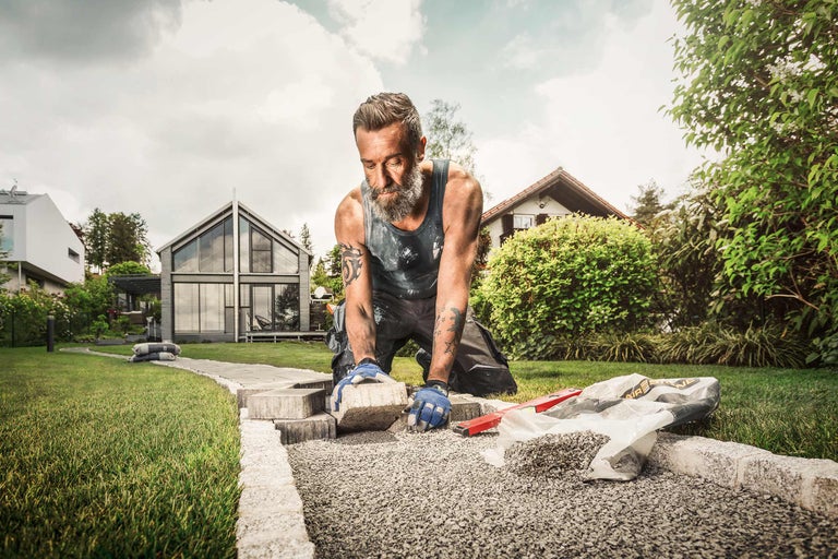 Mann verlegt Pflastersteine im Garten