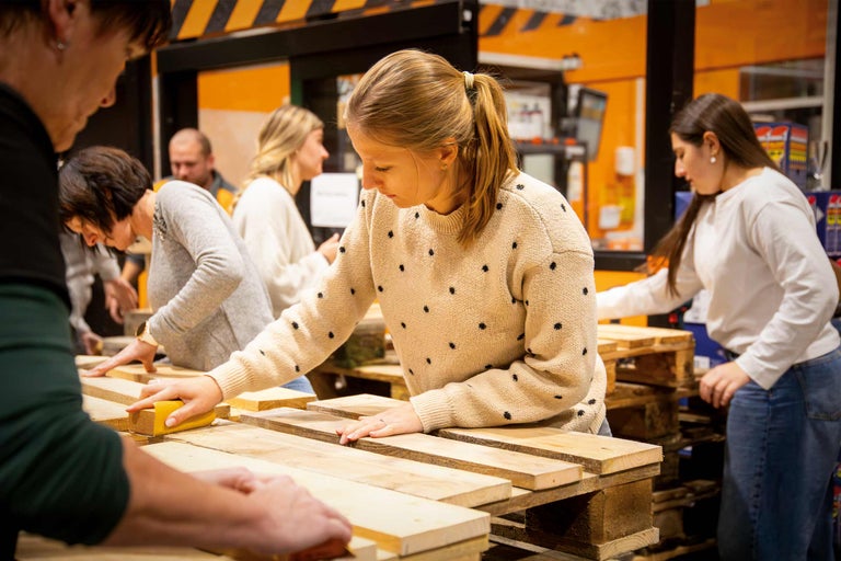 Mehrere Personen bearbeiten Holzpaletten mit Schleifpapier.