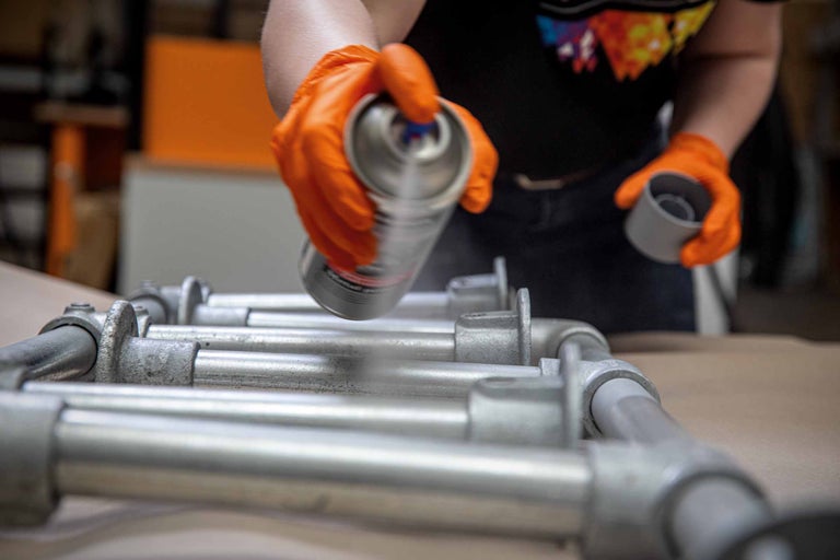Une personne portant des gants vaporise de la peinture sur une construction tubulaire.