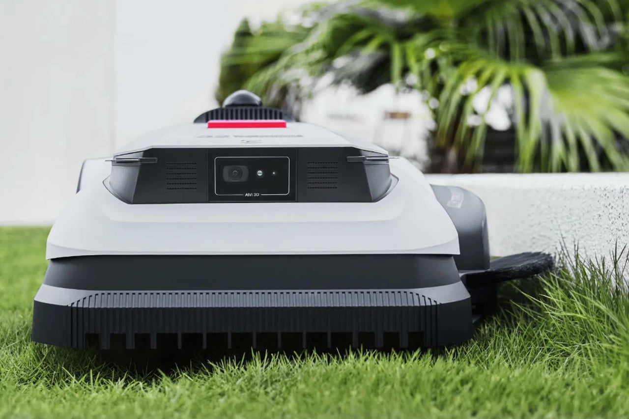 Robot tondeuse avec caméra AIVI 3D sur une pelouse devant des plantes.