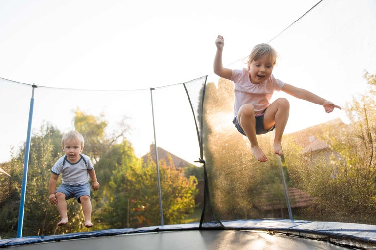 Deux enfants sautent sur un trampoline de jardin avec un filet de sécurité.