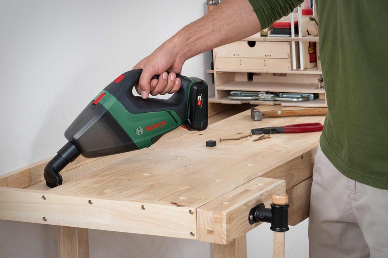 Un homme nettoie un établi avec un aspirateur à main sans fil Bosch