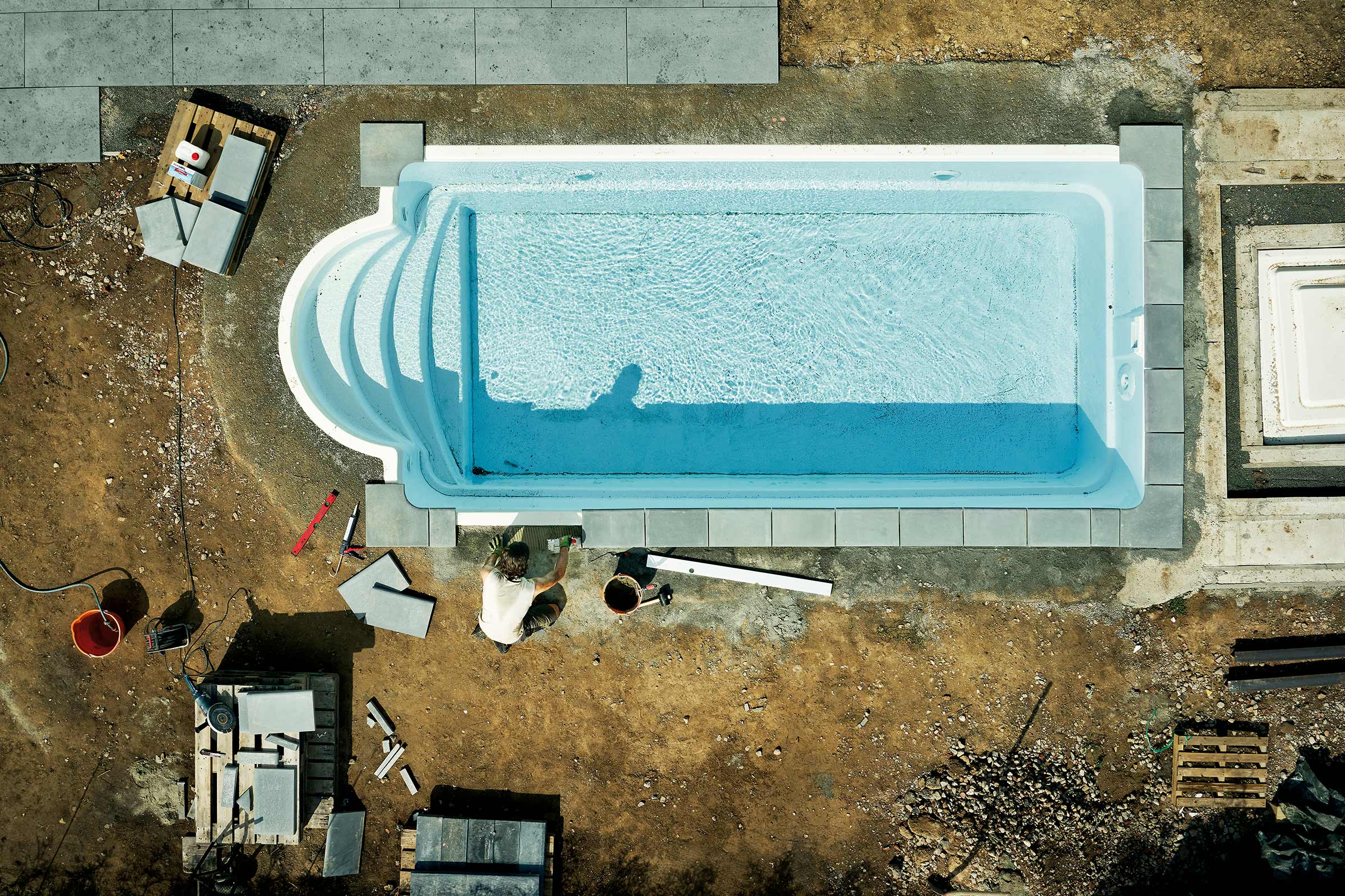 Aufbauszene eines Schwimmbeckens mit Wasser und umliegenden Pflastersteinen von oben.