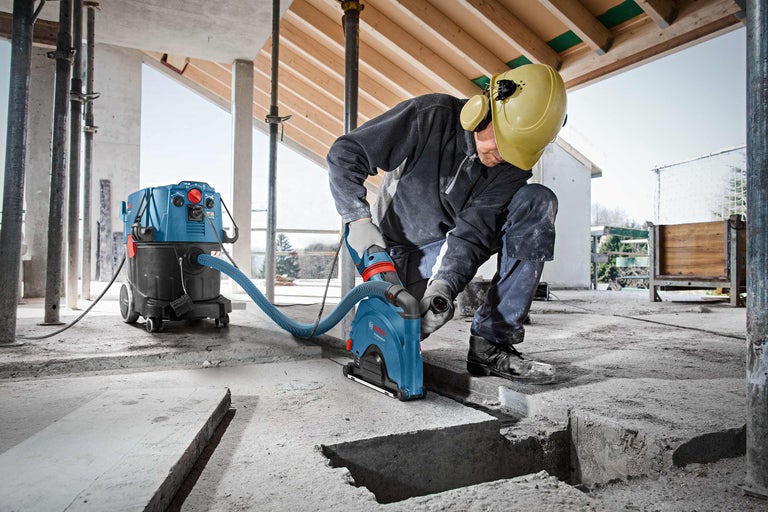 Un homme utilise une rainureuse à murs et un aspirateur industriel sur un chantier pour découper des rainures dans le sol en béton.