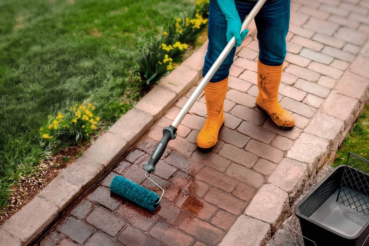Une personne applique un produit de scellement sur une allée pavée avec un rouleau avec Hornbach Logo et un manche télescopique.